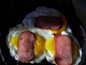 Crack three fresh eggs into the griddle, break the yolks, and top each with a thin slice of fried Spam.